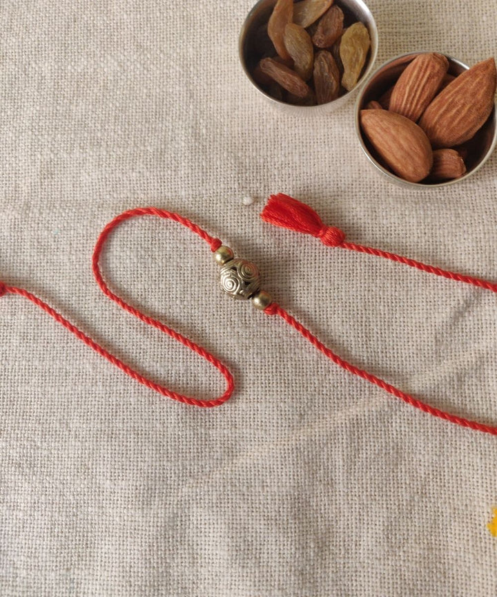 Handcrafted dhokra rakhi with red mercerised cotton thread