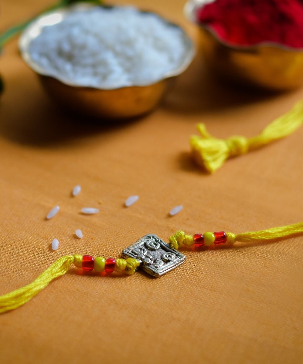 Handcrafted dhokra rakhi with yellow mercerised cotton thread