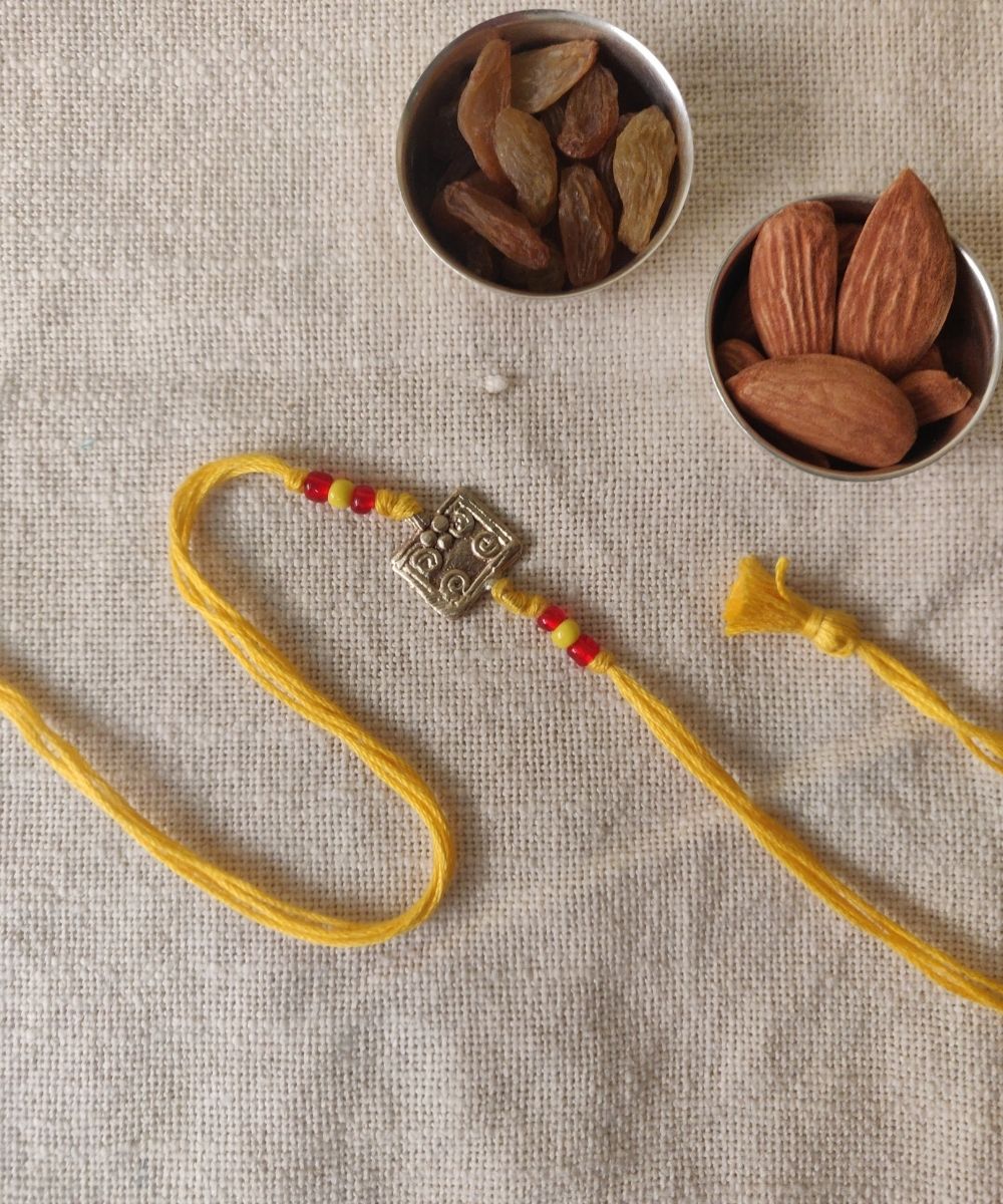 Handcrafted dhokra rakhi with yellow mercerised cotton thread