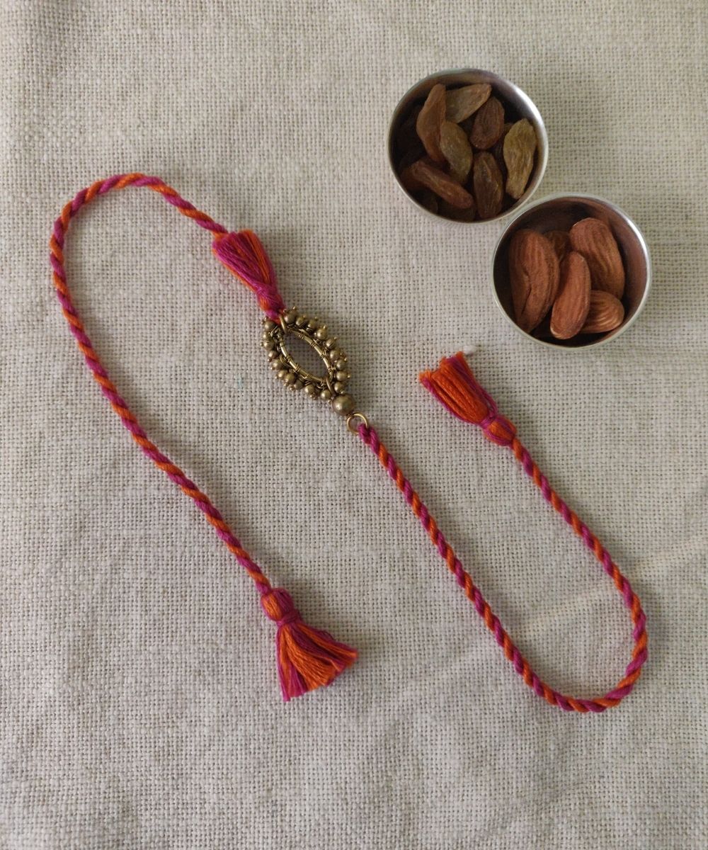 Handcrafted brass rakhi with pink orange mercerised cotton thread