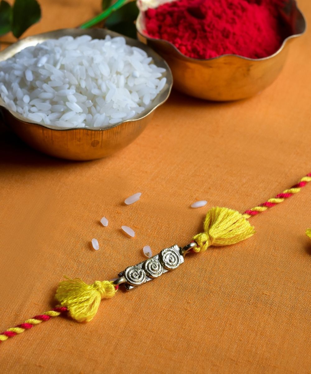 Handcrafted dhokra rakhi with red yellow mercerised cotton thread