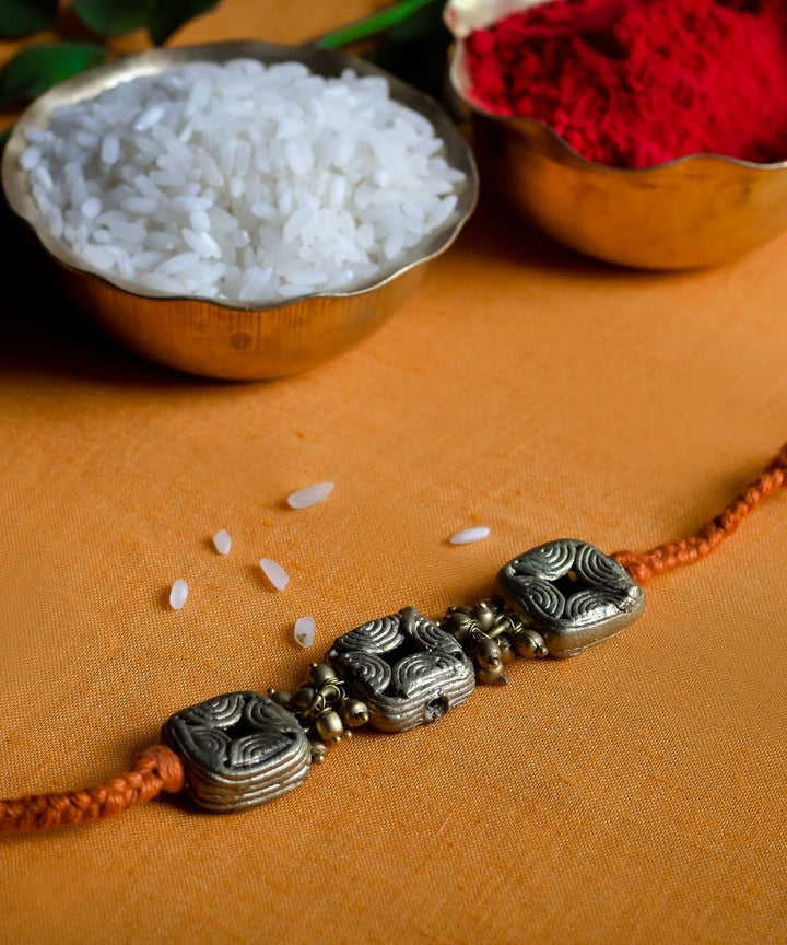 Hand crafted dhokra rakhi with orange mercerised cotton thread